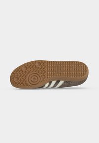 Λαστιχένια σόλα καφέ παπουτσιού Adidas με κυκλικά και τριγωνικά σχέδια πέλματος και τρεις λευκές ρίγες στο πλάι.