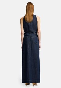 Robe maxi en denim bleu foncé avec un design sans manches, fente à l'arrière et deux poches arrière. Présente une taille définie et des accents de couture.