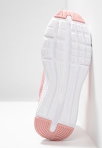 Suola di una scarpa sportiva rosa e bianca con un design di battistrada testurizzato, appoggiata contro una parete e una superficie bianche.
