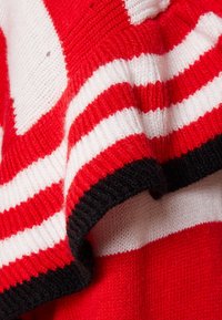 Pull en maille avec rayures horizontales rouges et blanches, bordé de côtes noires. Texture douce avec un travail de point bien marqué.