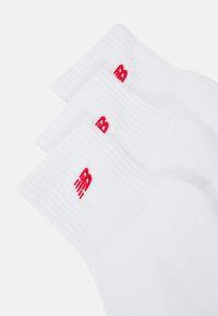 Chaussettes en coton blanc avec des bords côtelés et un petit logo rouge brodé sur chaque chaussette. Les chaussettes sont conçues pour le confort et la durabilité.