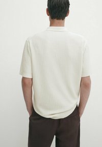 Kortærmet polo shirt i struktureret cremet stof, med et ribbet design og en klassisk krave, der er parret med brune bukser.