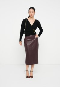 Suéter preto envolvente com três botões dourados na frente, combinado com uma saia de couro bordô justa até ao joelho e sapatos de salto preto com tiras.