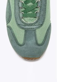 Sneaker verde caratterizzato da una combinazione di suede e tessuto, superficie testurizzata, lacci sottili e punta arrotondata con suola in gomma.