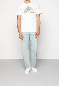 Camiseta corta de algodón blanca con un gráfico colorido, jeans de mezclilla azul claro y zapatillas blancas. Conjunto casual de corte relajado.