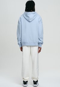 Felpa con cappuccio blu chiaro e vestibilità rilassata, con polsini a coste, abbinata a pantaloni bianchi e sneakers nere, vista dal retro.