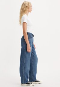 Szerokie niebieskie dżinsy wykonane z denimu, z wysokim stanem, wyblakłym wyglądem i klasycznym pięciokieszeniowym fasonem. Noszone z prostą białą koszulką.