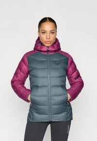 Μπουφάν με κουκούλα, με σώμα σε σκούρο τιρκουάζ χρώμα και μανίκια σε βαθύ ροζ. Καπιτονέ υφή, τσέπες με φερμουάρ και λογότυπο στο στήθος.
