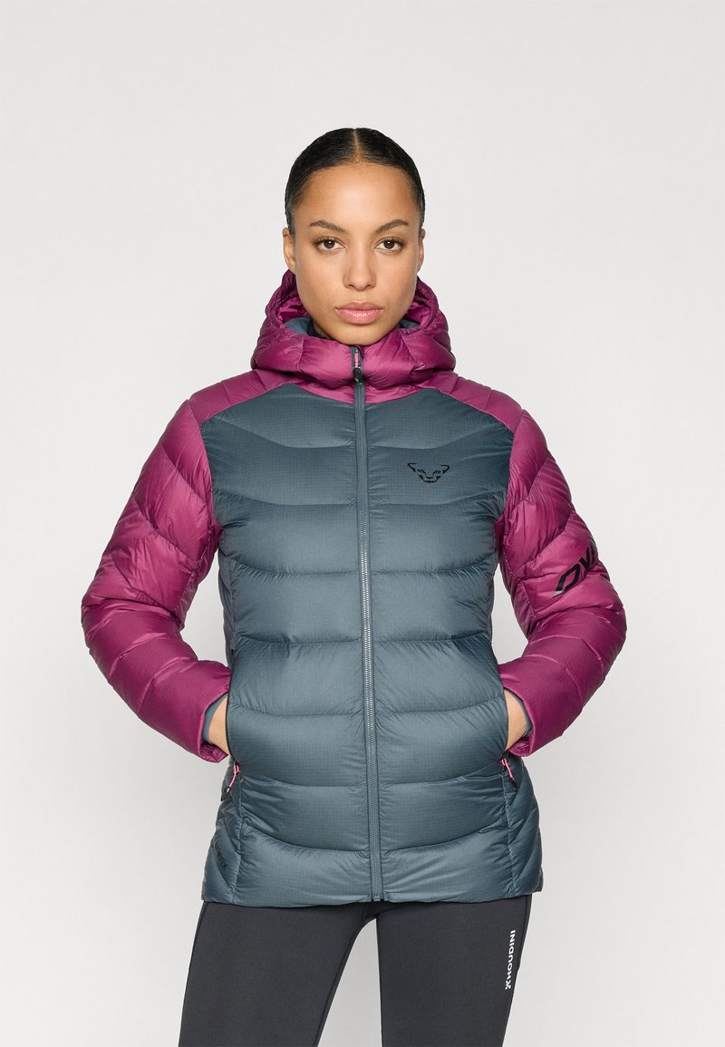 Μπουφάν με κουκούλα, με σώμα σε σκούρο τιρκουάζ χρώμα και μανίκια σε βαθύ ροζ. Καπιτονέ υφή, τσέπες με φερμουάρ και λογότυπο στο στήθος.