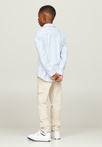 Camicia azzurra a righe, pantaloni cargo beige e sneakers bianche. La camicia ha maniche lunghe e i pantaloni presentano tasche laterali.