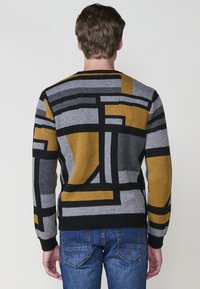 Suéter de punto con patrones geométricos en gris, negro y mostaza. Presenta un escote redondo y puños y dobladillo acanalados.