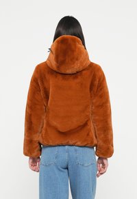Bruine fake fur hoodie jas met een zachte textuur, relaxte pasvorm en drop shoulders. Gepaard met hoge taille blauwe denim jeans.