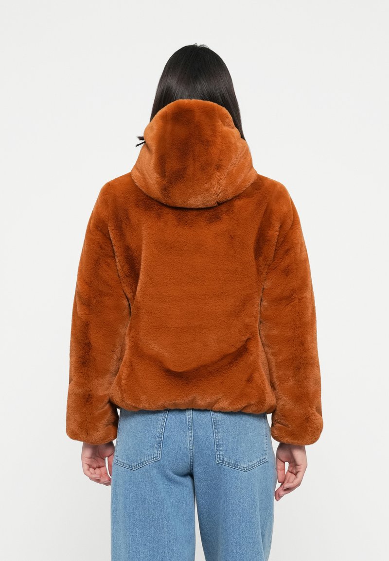 Bruine fake fur hoodie jas met een zachte textuur, relaxte pasvorm en drop shoulders. Gepaard met hoge taille blauwe denim jeans.