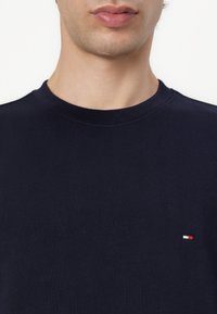 Navy blue crewneck sweatshirt made of cotton, featuring a small red, white, and blue logo on the left chest. Smooth texture, short sleeves.