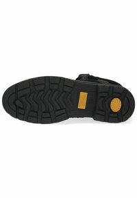Semelle extérieure en caoutchouc noir avec un motif de bande de roulement texturé, featuring un accent circulaire doré et un logo de marque visible. Robuste et conçu pour offrir une adhérence.