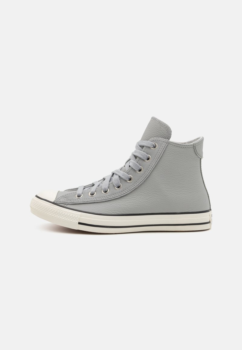 Adidași înalți din piele gri cu vârf și talpă din cauciuc alb. Prezintă șireturi gri și ochiuri metalice, cu detalii negre pe talpă.
