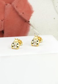 Orecchini a perno a forma di coccinella dorata con macchie nere e dettagli in cristallo. Texture liscia con una finitura lucida, forma compatta per un facile utilizzo.