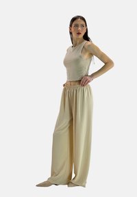Beige kort cropped tanktop en losse, hoogtaille broek van zachte stof. De outfit heeft een ontspannen silhouet en een elastische tailleband.