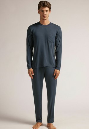 Donkerblauw pyjama set met lange mouwen, gemaakt van zachte stof; heeft een borstzak en aansluitende, taps toelopende broeken met elastische manchetten.