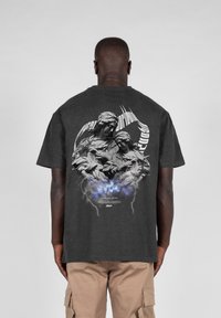 Mørkegrå bomulds t-shirt med et grafisk print af to figurer med komplekse detaljer og svirvlende tekst, akkompagneret af blå og grå effekter.