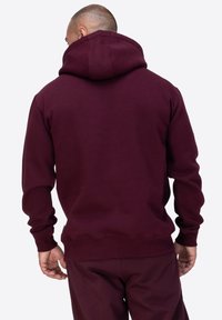 Burgundowa bluza z luźnym krojem, z dużym kapturem z tyłu, prążkowanymi mankietami i pasem, wykonana z miękkiej, strukturalnej tkaniny.