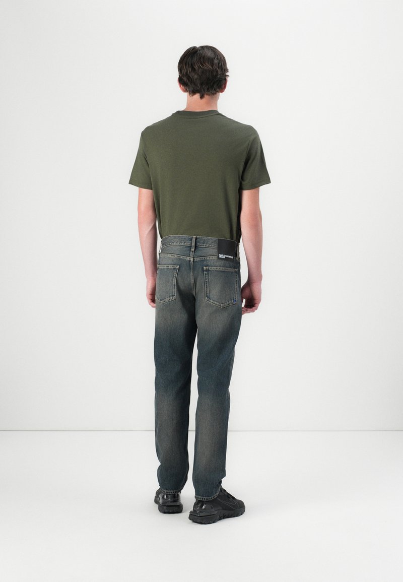 Olive green T-shirt, back view, paired with dark denim jeans featuring a straight cut and two back pockets. Worn with black sneakers.
