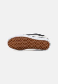 Semelle d'une basket noir et blanc avec un motif gaufré en caoutchouc marron sur fond blanc.