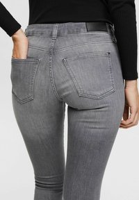 Gray slim-fit jeans with a smooth texture, two back pockets, and a black waistband. The fabric has a soft, worn appearance.