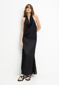 Black satin halter top with draped neckline paired with a long black skirt featuring lace accents at the sides. Flat strappy sandals.