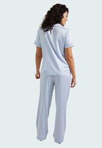 Conjunto de pijama de color azul claro, de manga corta, que incluye una camisa con cuello y borde de encaje, y pantalones holgados con acentos de encaje a juego en los puños.