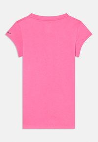 T-shirt à manches courtes en coton rose vif. Texture lisse avec un col rond et un petit logo sur la manche gauche.