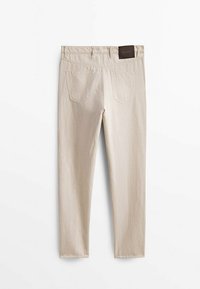 Beige farkut slim fit -mallissa, joissa on kaksi takataskua ja teksturoitu ruskea vyömerkki. Mattapintainen viimeistely pehmeällä tekstuurilla.