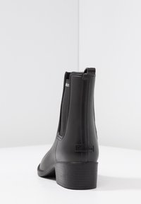 Bottines noires en matériau synthétique lisse, avec panneaux latéraux élastiques, talon bas et logo au dos. Design simple et forme épurée.