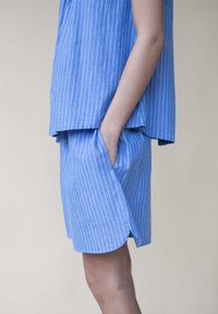 Hellblau gestreiftes Oberteil und Shorts-Set. Das Oberteil hat eine lockere Passform; die Shorts verfügen über seitliche Taschen. Das Material scheint atmungsaktiv und hat eine glatte Textur.