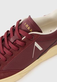 Maroon sneaker with textured leather, white accent logo, and round laces. Light-colored sole with subtle tread pattern and cushioned interior.