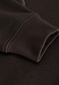 Tela de sudadera marrón oscuro con un primer plano del borde acanalado del puño, que presenta una textura suave y detalles de diseño minimalistas.