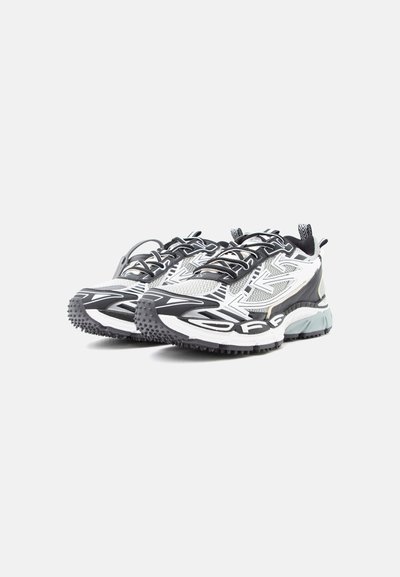 Ζευγάρι αθλητικά παπούτσια σε μαύρο, λευκό και γκρι, με παχιά σόλα και υφή στην εξωτερική σόλα, εμφανιζόμενα από μπροστινή-πλευρική γωνία σε λευκό φόντο.