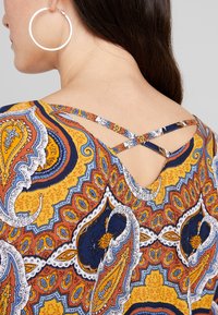 Mønstret top i flere farver med et gult, blåt og oranget paisley-design, der har et krydset stropdetalje på ryggen.