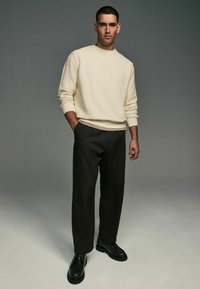 Beige tekstureret sweater, sorte bukser og sorte sko. Sweateren har ribbede manchetter, en lige pasform og en minimalistisk stil.