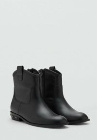 Botas negras hasta el tobillo con cremallera lateral, tiradores y detalles metálicos en forma de estrella en los bajos, mostradas sobre un fondo claro y liso.