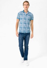 Kortærmet blå polo t-shirt med et struktureret mønster, parret med slidte mørkeblå jeans og hvide sneakers.