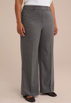 Femme portant un pantalon gris à fines rayures, taille haute et jambes larges, avec un bouton et une fermeture éclair, associé à des ballerines en mesh noires et un haut blanc.