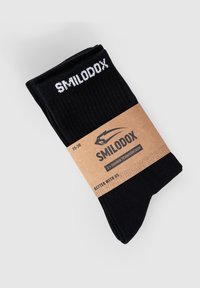 Calcetines de color negro con relieve que presentan el nombre de la marca "SMILODOX" en texto blanco. Envueltos con una banda de cartón marrón que muestra la información de tallas.