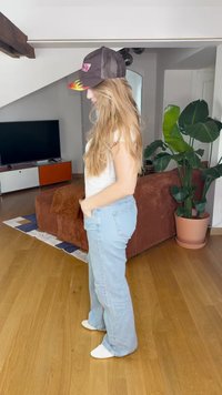 Gai zilu izplešotās džinsa bikses ar aizmugurējām kabatām; baltā piegulošā T-kreklā; melns cepure ar liesmu dizainu; saskaņots ar baltām zeķēm.