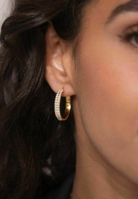 Goldene Creole mit einer Reihe klarer, funkelnder Kristalle an der Vorderseite. Glatte Oberfläche mit polierter Textur.