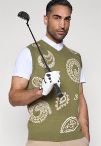 Žalias mezgintas liemenėlis su kreminiais paislių raštais, derinamas su balta marškinių apykakle. Figūra laiko golfo klubą, dėvi baltą pirštinę.