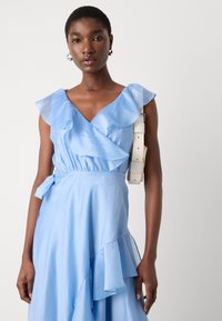 Light blue dress featuring ruffled sleeves and a wrap design with a flared hem. Canvas belt accentuating the waist. Silky texture.
