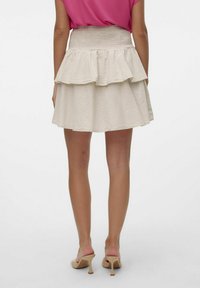 Gonna a strati beige con una vita aderente arricciata, realizzata in un tessuto morbido, con un orlo ondulato, abbinata a décolleté color nude.