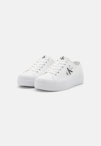 Weiße Leinensneaker mit einem Low-Top-Design, ausgestattet mit einer strukturierten Plattformsohle und metallischen Ösen, akzentuiert durch ein Logo an der Seite.