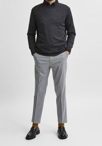 Mörkgrå tröja med långa ärmar, ljusgrå skräddarsydda byxor, svarta loafers och senapsgula strumpor. En enkel, modern design.